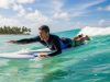 Surfer wearing a long-sleeve rash guard paddling on a surfboard in tropical water