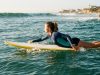 Surfer wearing a rash guard and anti-chafing swimwear paddling out on a surfboard in the ocean
