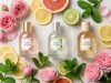Three perfume bottles arranged neatly on linen fabric next to fresh roses and sliced citrus.