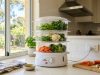 A modern electric food steamer filled with fresh vegetables on a kitchen counter.