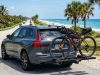 A platform hitch bike rack mounted on an SUV near a sunny coastal road.