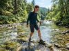 Person trying on durable water shoes by a rocky riverbank.