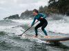 Paddleboarder gliding across calm coastal waters under a sunny California sky.